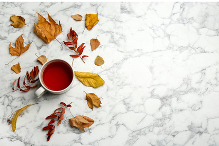 Flat lay composition with cup of hot drink and autumn leaves on white marble background, space for text. Cozy atmosphereの写真素材