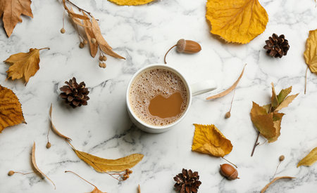 Flat lay composition with cup of hot drink and autumn leaves on white marble background. Cozy...