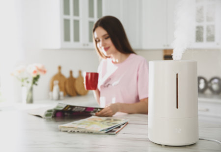 Modern air humidifier and blurred woman drinking coffee in kitchenの写真素材