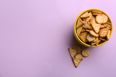 Delicious crackers in bowl on violet background, flat lay. Space for textの写真素材