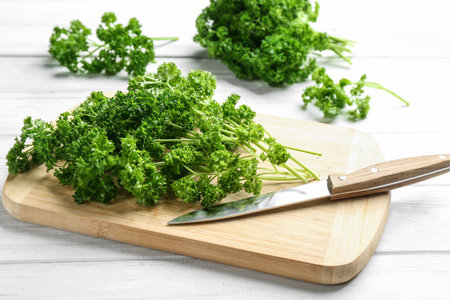 Fresh curly parsley, cutting board and knife on white wooden tableの写真素材