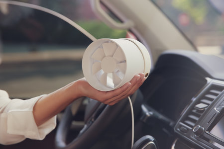 Woman with portable fan in car on hot summer day, closeup