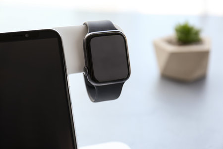 Stylish smart watch and phone charging with wireless pad against blurred background, closeup. Space...