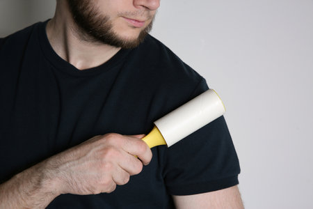 Man cleaning black t-shirt with lint roller on white background, closeupの写真素材