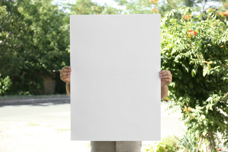 Man holding white empty poster outdoors. space for designの写真素材