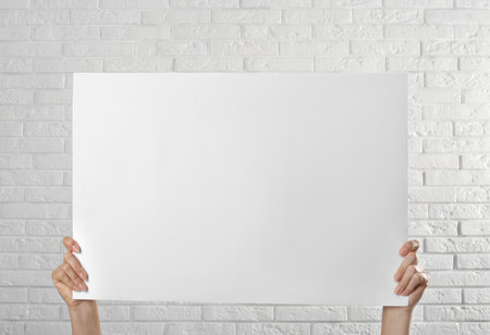 Woman holding blank poster near white brick wall, closeup. Mockup for designの写真素材