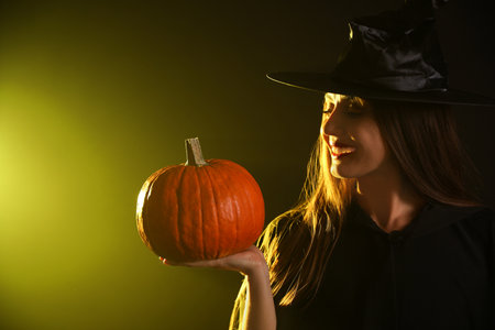 Young woman wearing witch costume with pumpkin on dark background. Halloween partyの写真素材