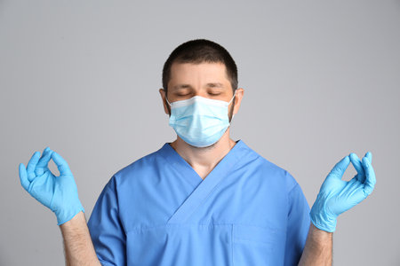 Doctor in protective mask meditating on gray background. Dealing with stress caused by COVID?19 pandemicの写真素材