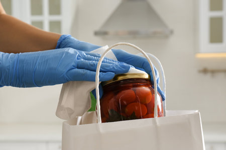 Woman cleaning newly purchased jar of pickled tomatoes with antiseptic wipe indoors, closeup....