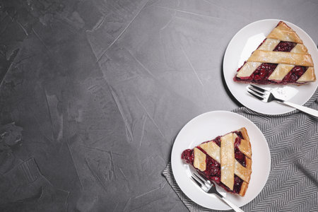 Slices of delicious fresh cherry pie served on gray table, flat lay. Space for text