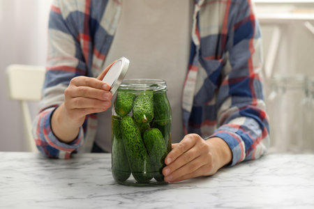 Woman pickling glass jar of cucumbers at white marble kitchen table, closeupの写真素材