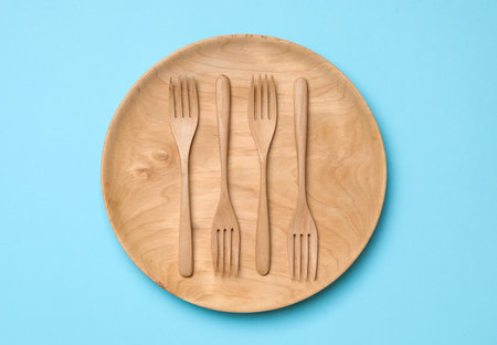 Wooden plate with forks on light blue background, top view. Cooking utensilsの写真素材
