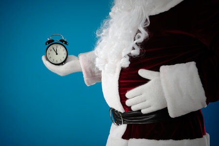 Santa Claus holding alarm clock on blue background, closeup. christmas count downの写真素材