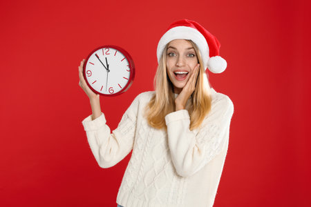 Woman in Santa hat with clock on red background. New Year count downの写真素材