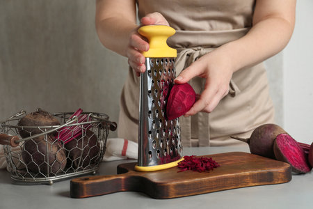 Woman grating fresh red beet at table, closeupの写真素材
