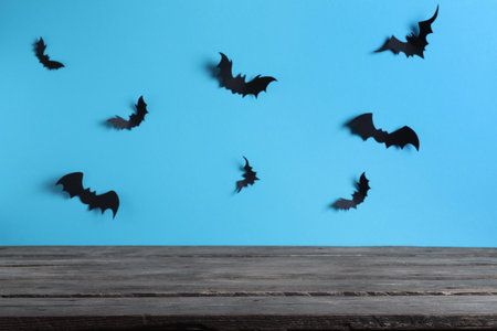 Empty wooden table near light blue wall decorated with paper bats. halloween celebrationの写真素材