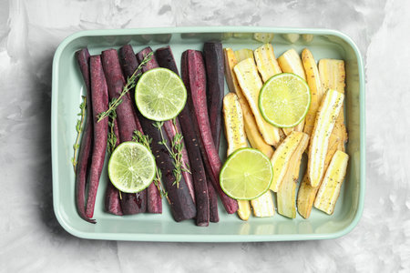 Raw black and white carrots with lime slices in baking dish on light gray table, top viewの写真素材