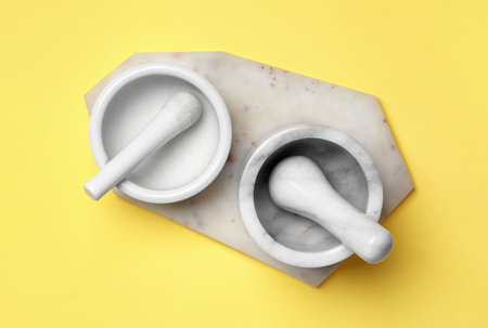 Ceramic mortars with pestles and marble board on yellow background, top view. Cooking utensilsの写真素材