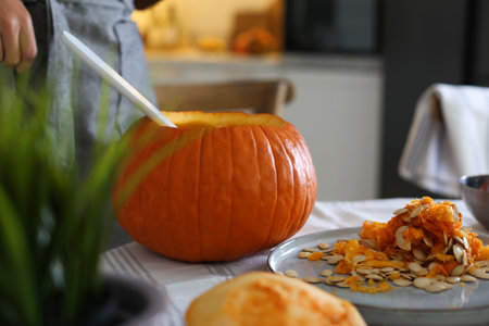 Woman making pumpkin jack o'lantern at table indoors. halloween celebrationの写真素材