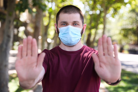 Man in protective face mask showing stop gesture outdoors.
