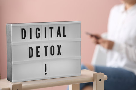 Woman using smartphone against pink background, focus on lightbox with phrase DIGITAL DETOXの写真素材