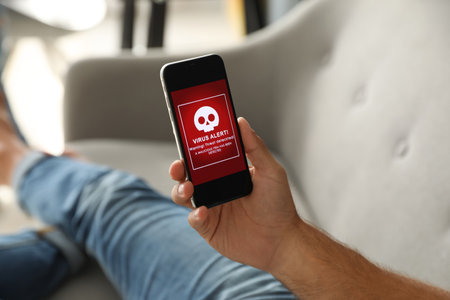 Man holding smartphone with warning about virus attack at home, closeup