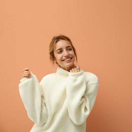 Beautiful young woman wearing knitted sweater on light brown backgroundの写真素材