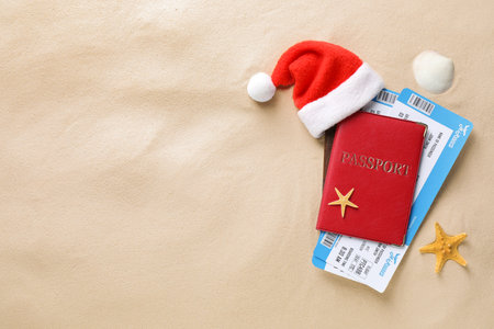 Passport with tickets, Santa hat, seashell, starfish and space for text on sand, flat lay. christmas holidaysの写真素材