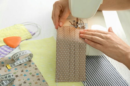 Woman sewing cloth mask with machine at table, closeup. Personal protective equipment during...