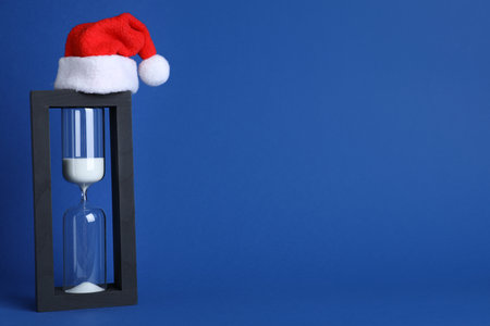 Hourglass and Santa hat on blue background, space for text. christmas count downの写真素材