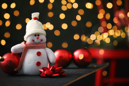 Cute snowman, bow and Christmas balls on table, bokeh effect. Space for textの写真素材