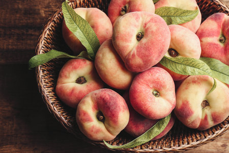 Fresh ripe donut peaches in basket on wooden table, top viewの写真素材