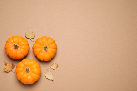 Fresh ripe pumpkins and autumn leaves on brown background, flat lay. Space for text