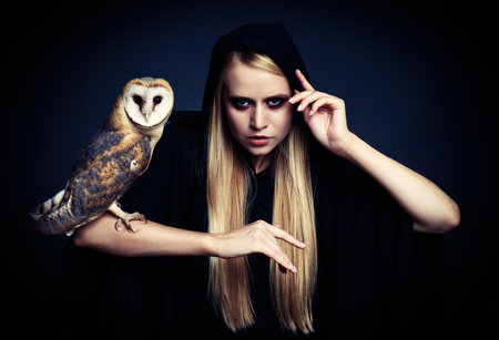 Witch in black mantle with owl on dark background. Scary fantasy characterの写真素材