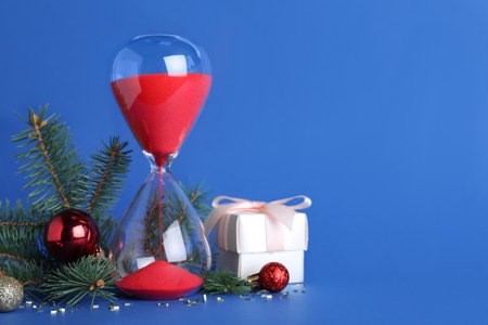Hourglass, gift, fir tree branches with decor on blue background, space for text. christmas count...