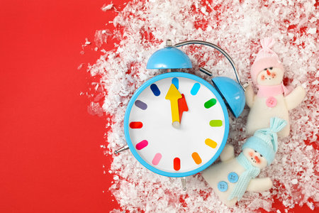 Alarm clock and snowmen in pile of snow on red background, flat lay with space for text. New Year countdownの写真素材