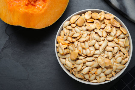 Raw seeds and fresh pumpkin on black slate table, flat lay. Space for textの写真素材