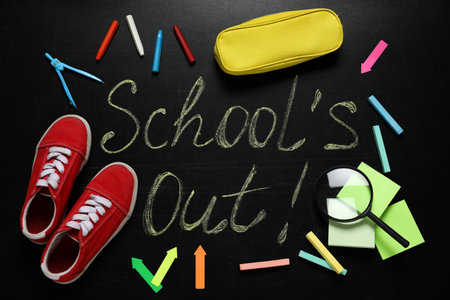 Shoes, stationery and text SCHOOL'S OUT written on blackboard, flat lay. summer holidays