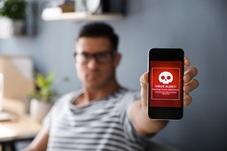 Man holding smartphone with warning about virus attack at home, focus on hand