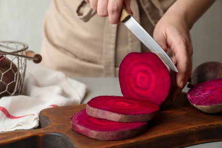 Woman cutting fresh red beet at table, closeup
