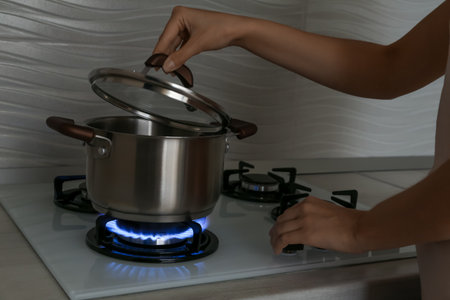 Woman near gas stove with pot in kitchen, closeupの写真素材