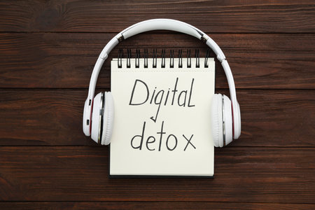 Notebook with phrase DIGITAL DETOX and headphones on wooden table, flat layの写真素材