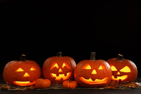 Glowing jack o'lanterns on table in darkness, space for text. halloween decor