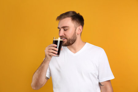 Handsome man with cold kvass on yellow background. Traditional Russian summer drinkの写真素材