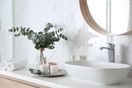 Fresh eucalyptus branches and burning candles on countertop in bathroomの写真素材