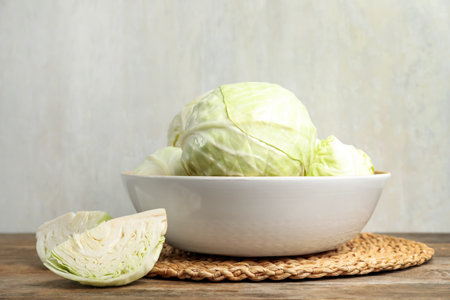 Fresh whole and cut cabbages in bowl on wooden tableの写真素材