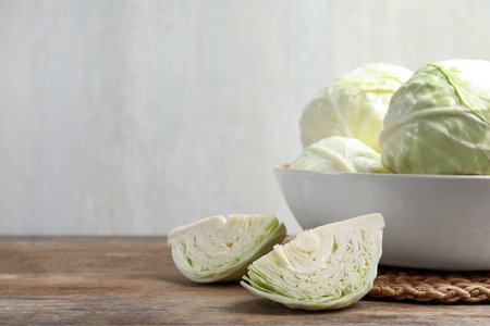 Fresh whole and cut cabbages in bowl on wooden table. Space for textの写真素材