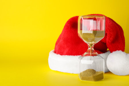 Hourglass and Santa hat on yellow background, space for text. christmas count downの写真素材