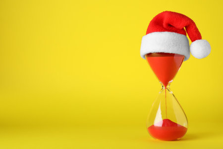 Hourglass and Santa hat on yellow background, space for text. christmas count downの写真素材
