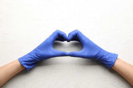 Person in medical gloves showing heart gesture on white wooden background, closeup of handsの写真素材